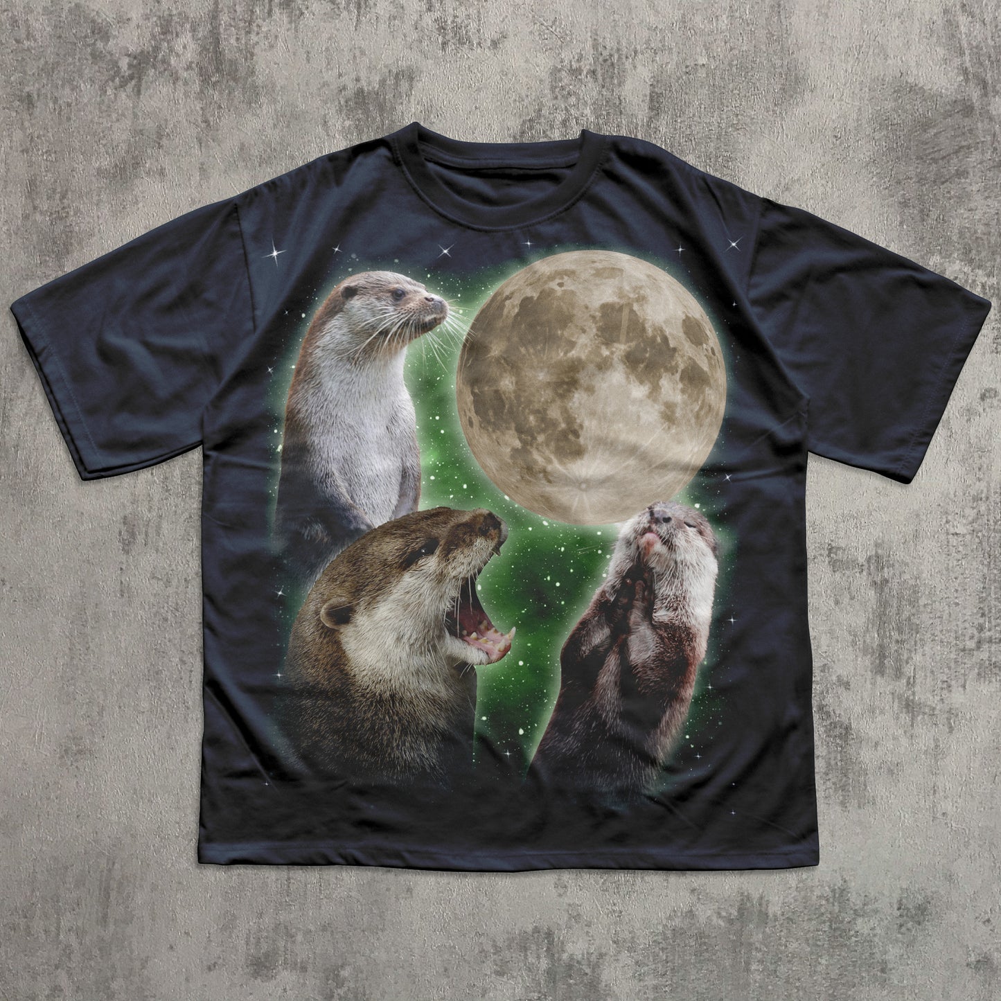 Black t-shirt with graphic of three otters and a moon on a textured gray background