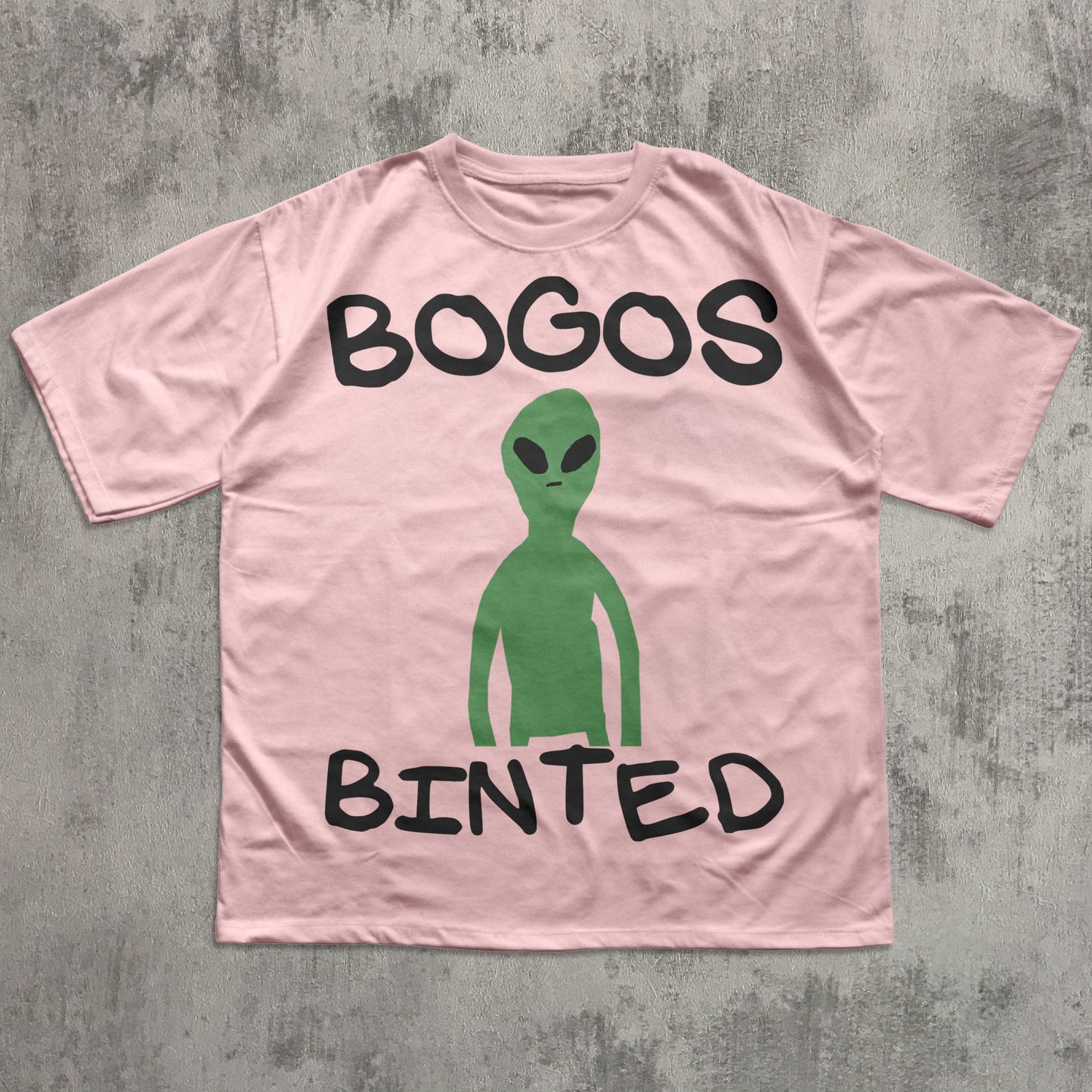Pink t-shirt with a green alien graphic and text on a gray textured background