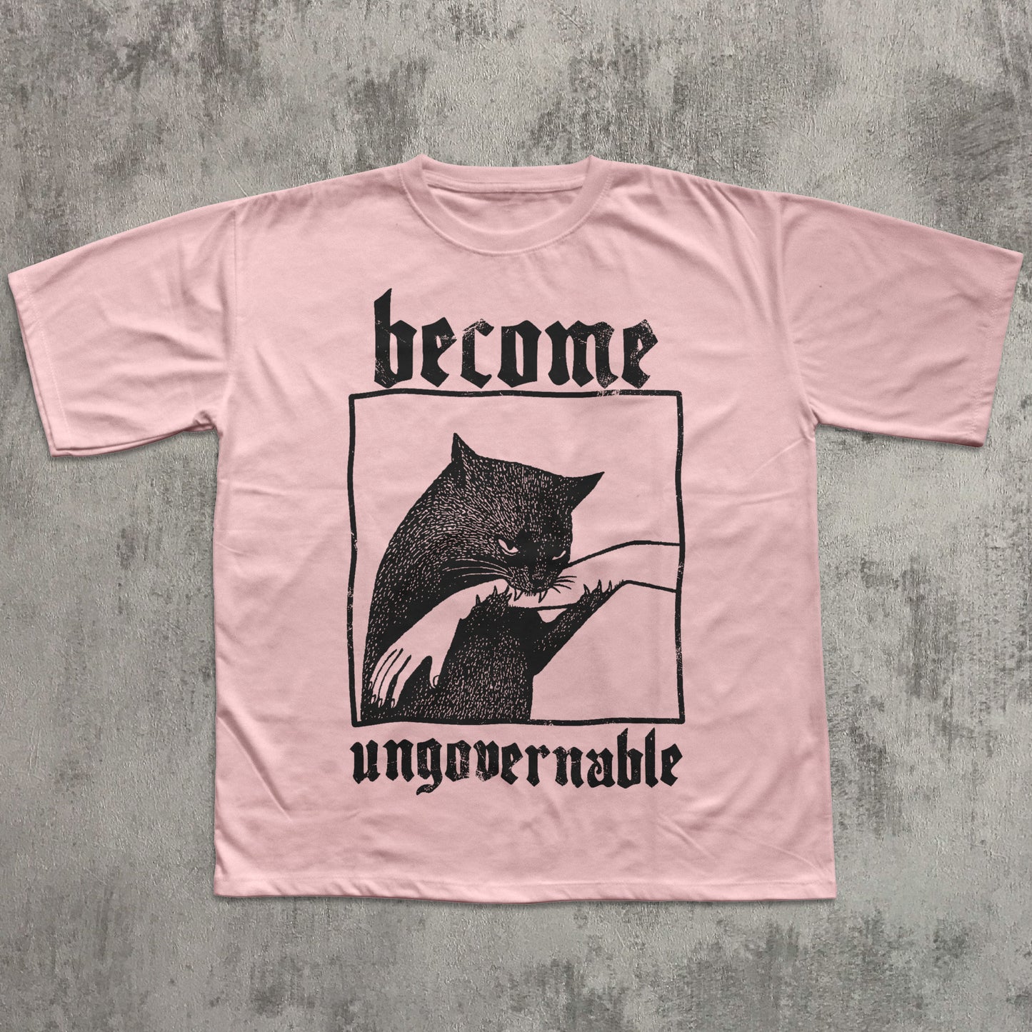 Pink t-shirt with black graphic and text 'become ungovernable' on a textured gray background