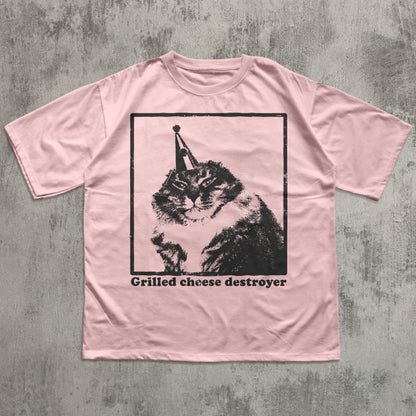 Pink t-shirt with a graphic of a cat and text 'Grilled cheese destroyer' on a textured gray background