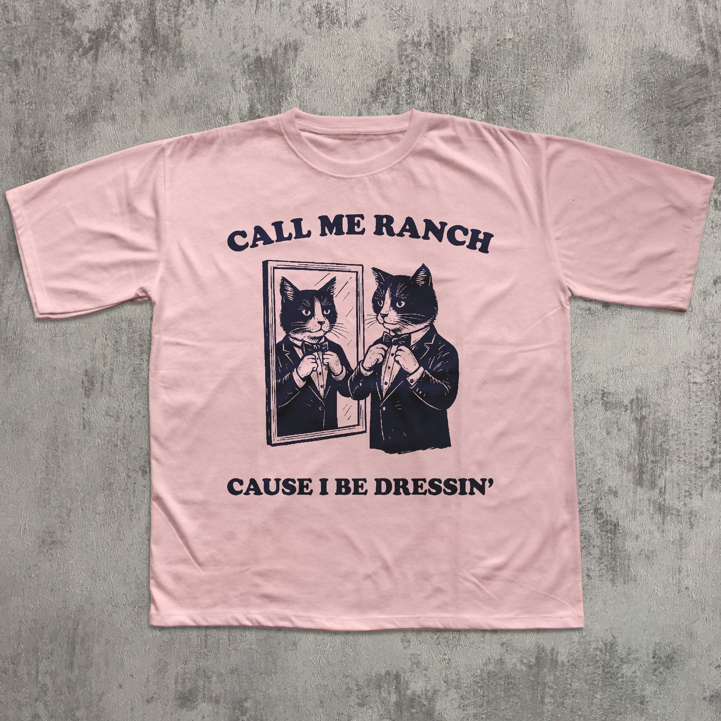 Pink t-shirt with black cat graphic and text on a gray concrete background