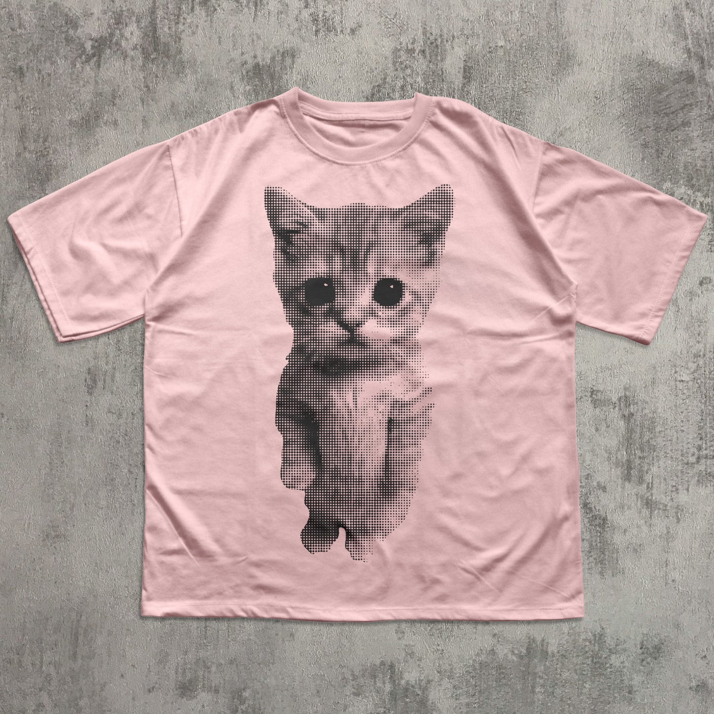Pink t-shirt with a black and white kitten graphic on a textured gray background