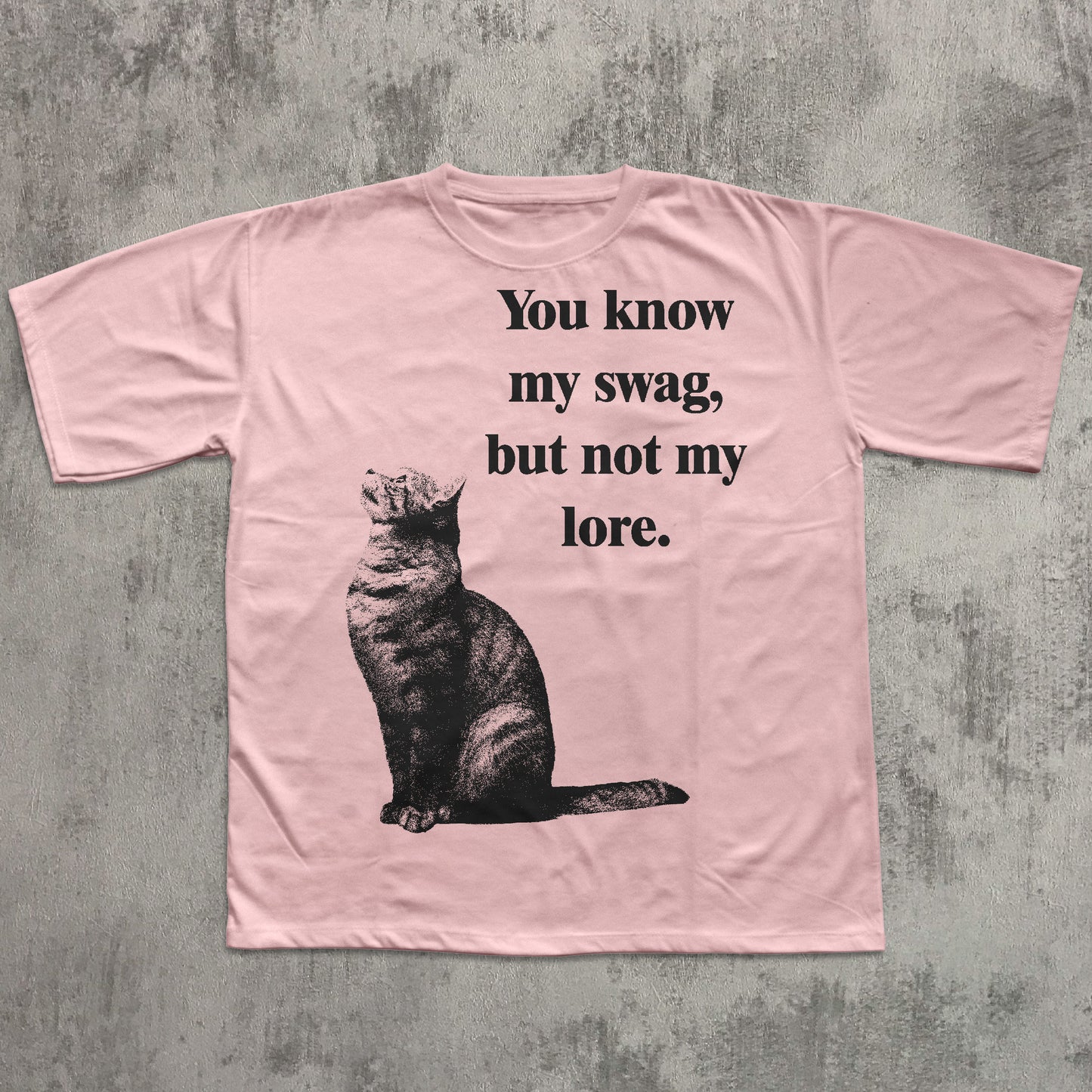 Pink t-shirt with a cat graphic and text on a concrete surface