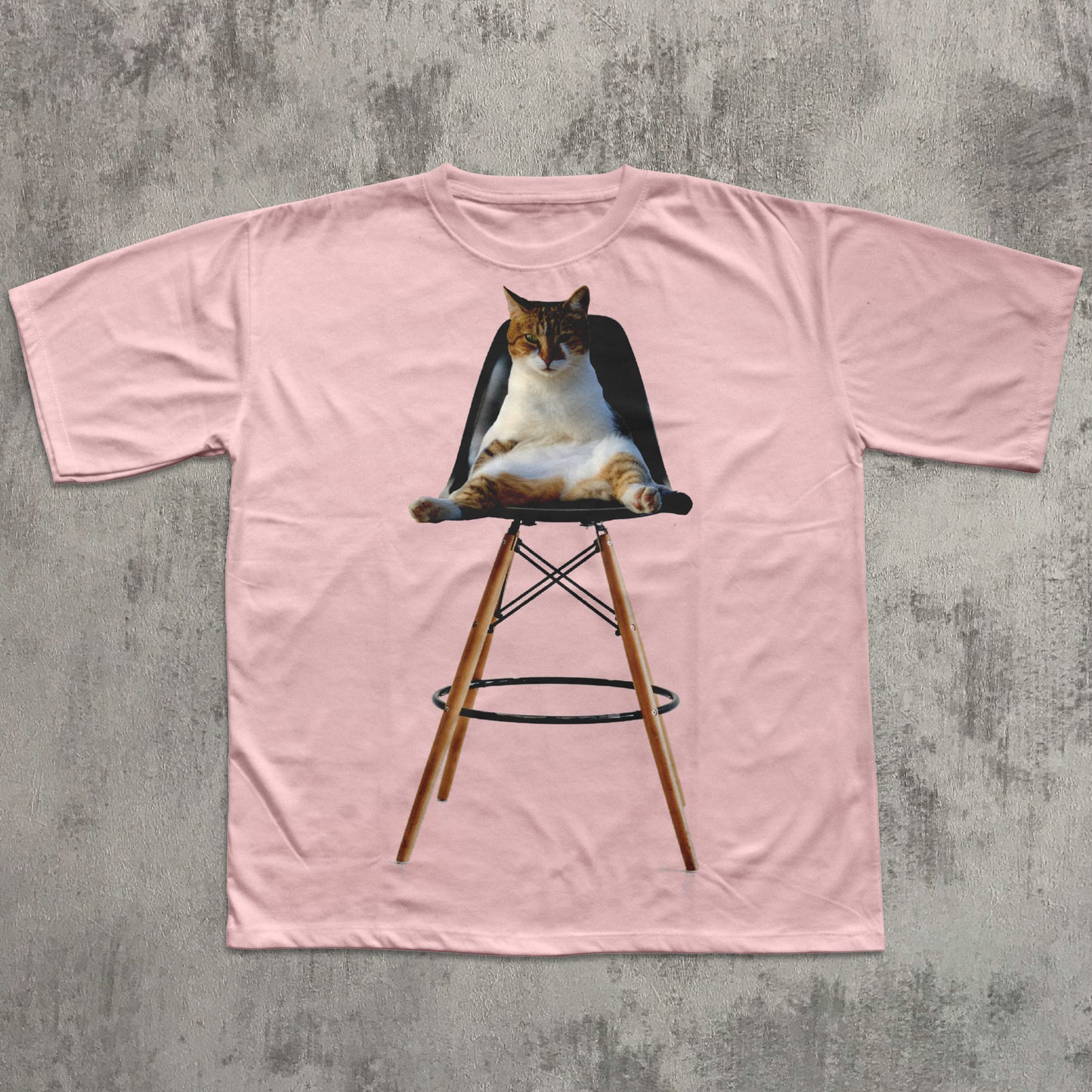 Pink t-shirt with a graphic of a cat on a stool against a concrete wall.
