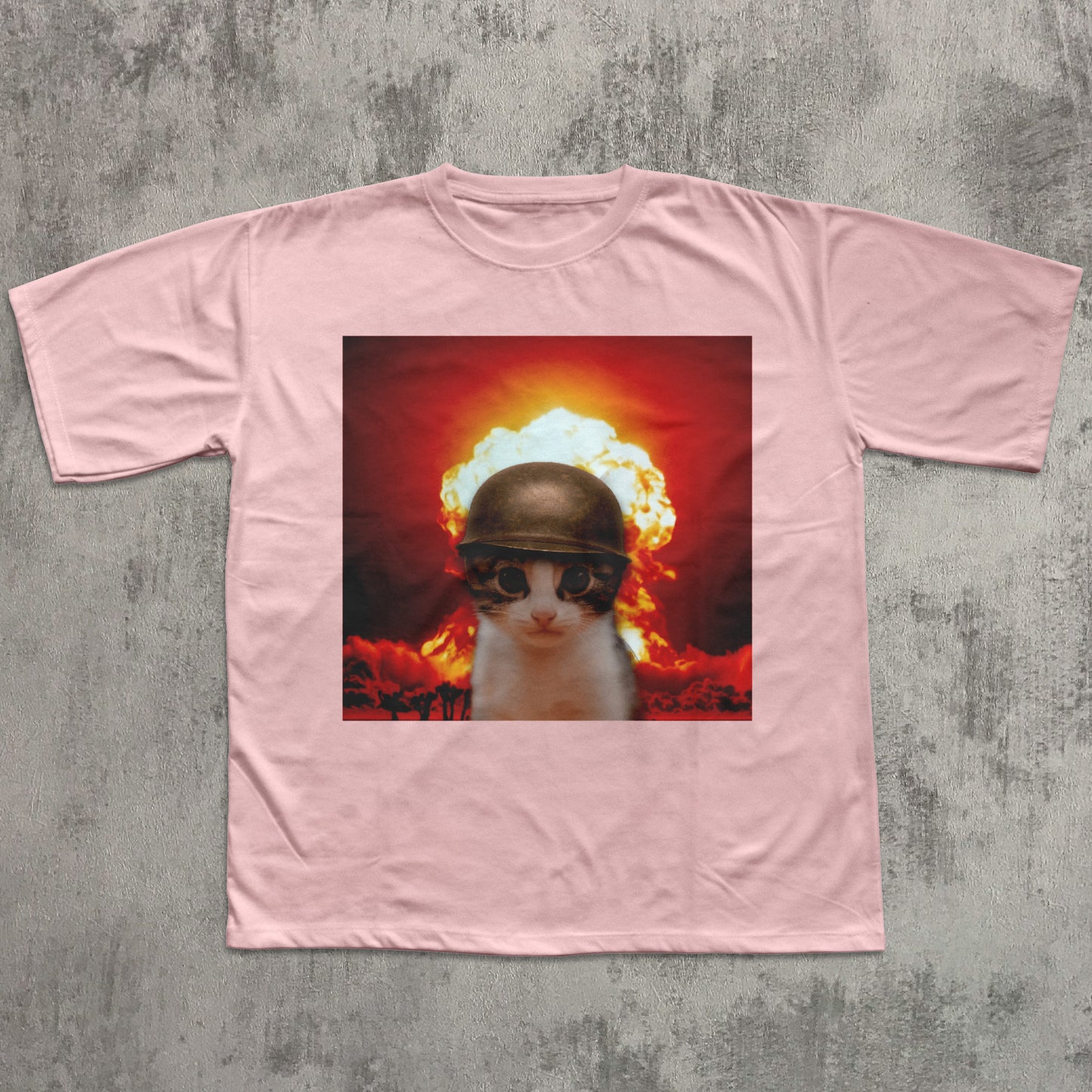 Pink t-shirt with a graphic of a cat wearing a helmet and goggles in front of an explosion on a concrete floor.