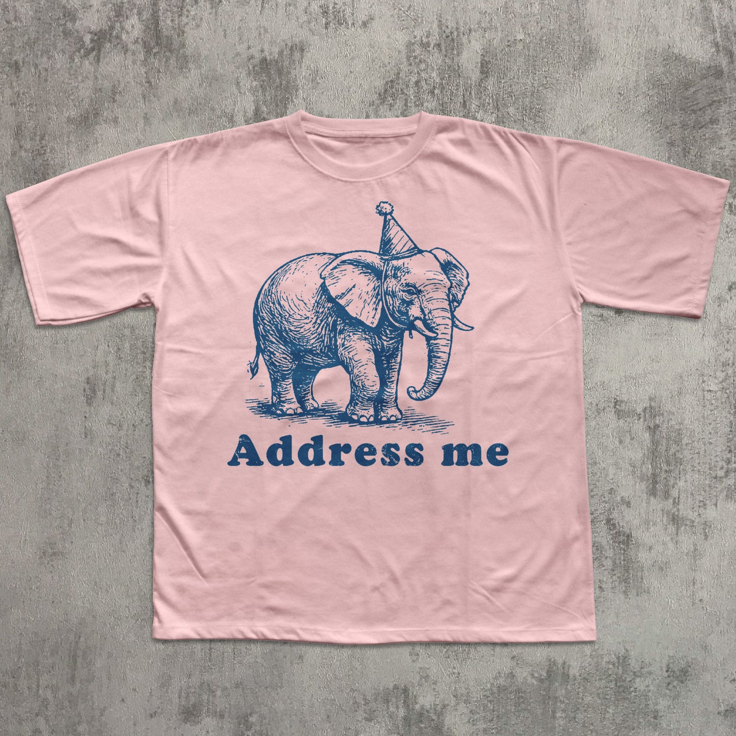 light pink t-shirt with an elephant graphic and 'Address me' text on a textured gray background