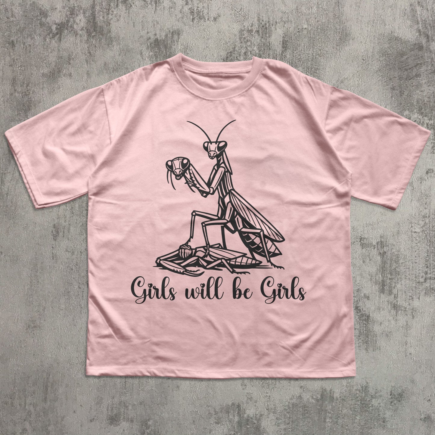 Pink t-shirt with a praying mantis graphic and text on a textured gray background