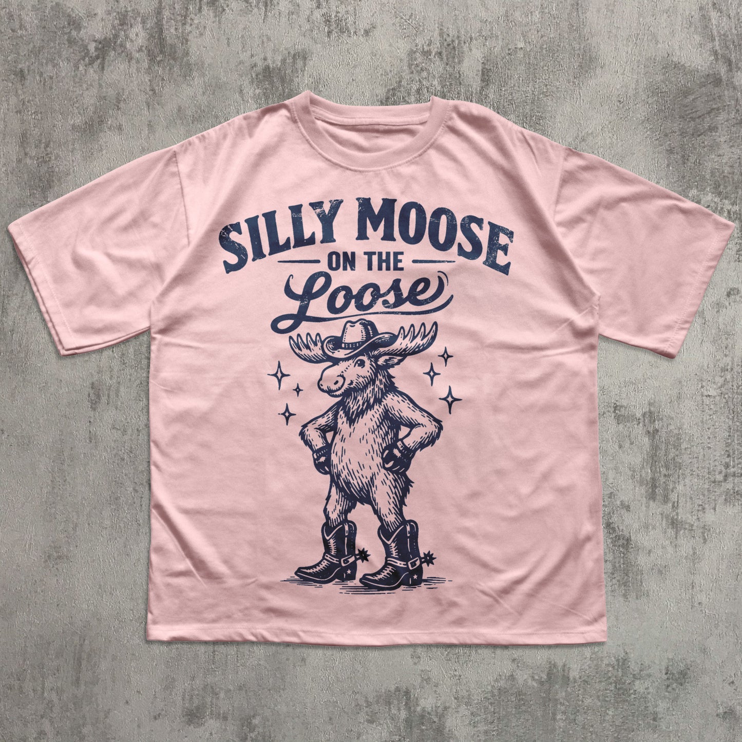 Pink t-shirt with a moose graphic and text 'Silly Moose on the Loose' on a textured gray background