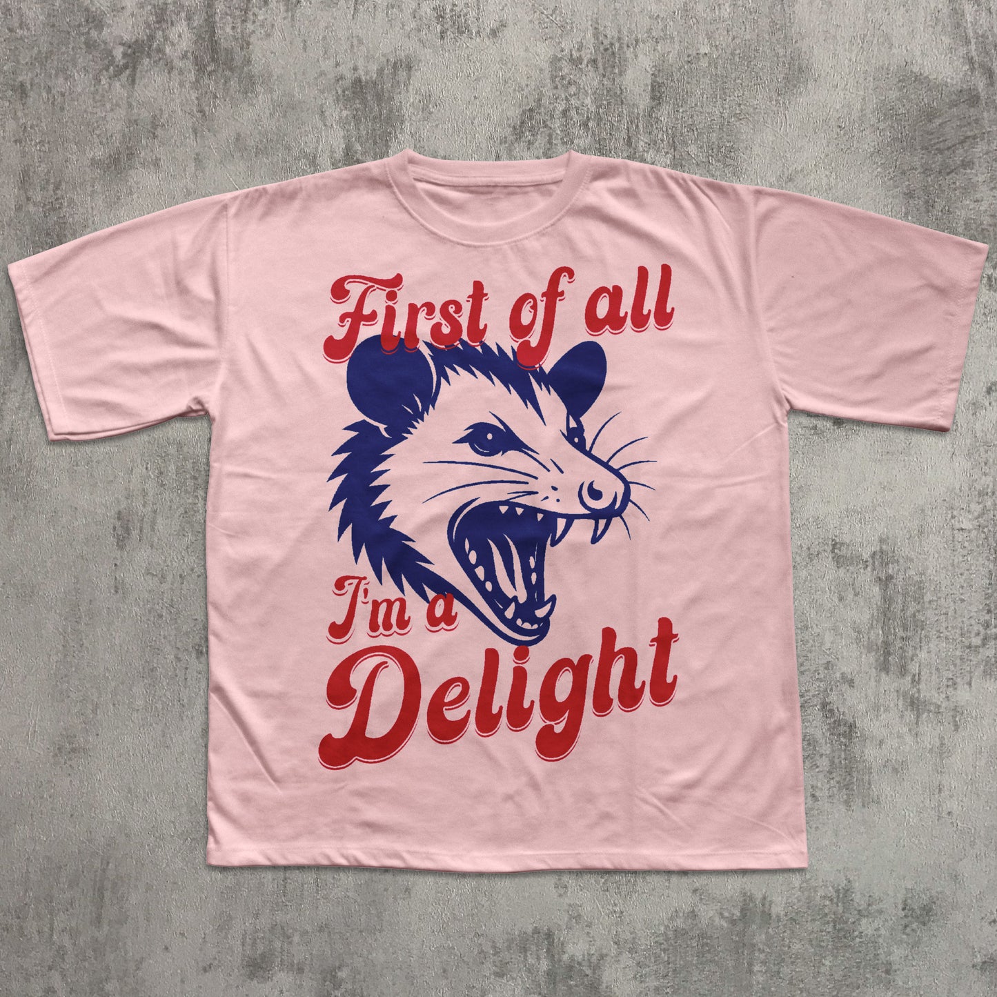 Pink t-shirt with a graphic of an opossum and text on a gray concrete background