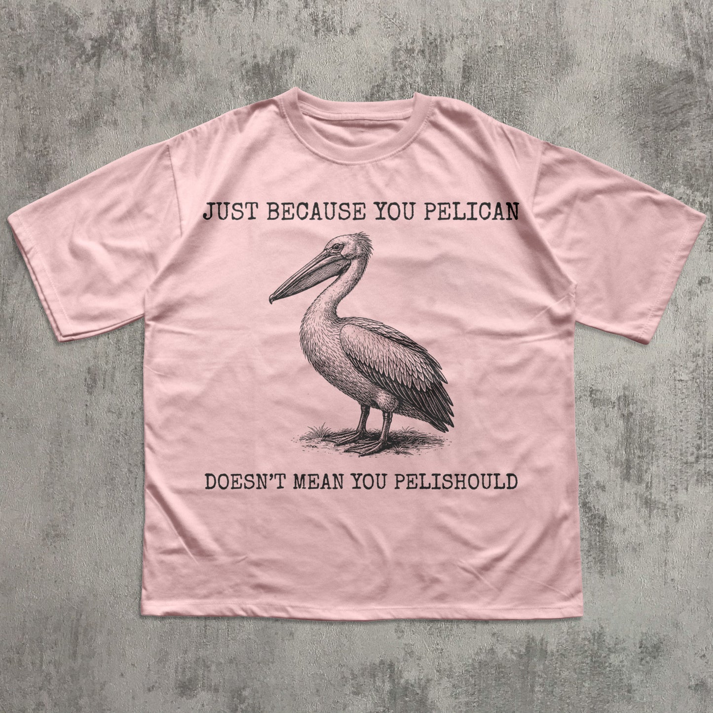 Pink t-shirt with a pelican graphic and humorous text on a textured gray background