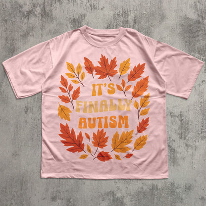 Pink t-shirt with autumn leaf design and 'It's Finally Autism' text on a textured gray background