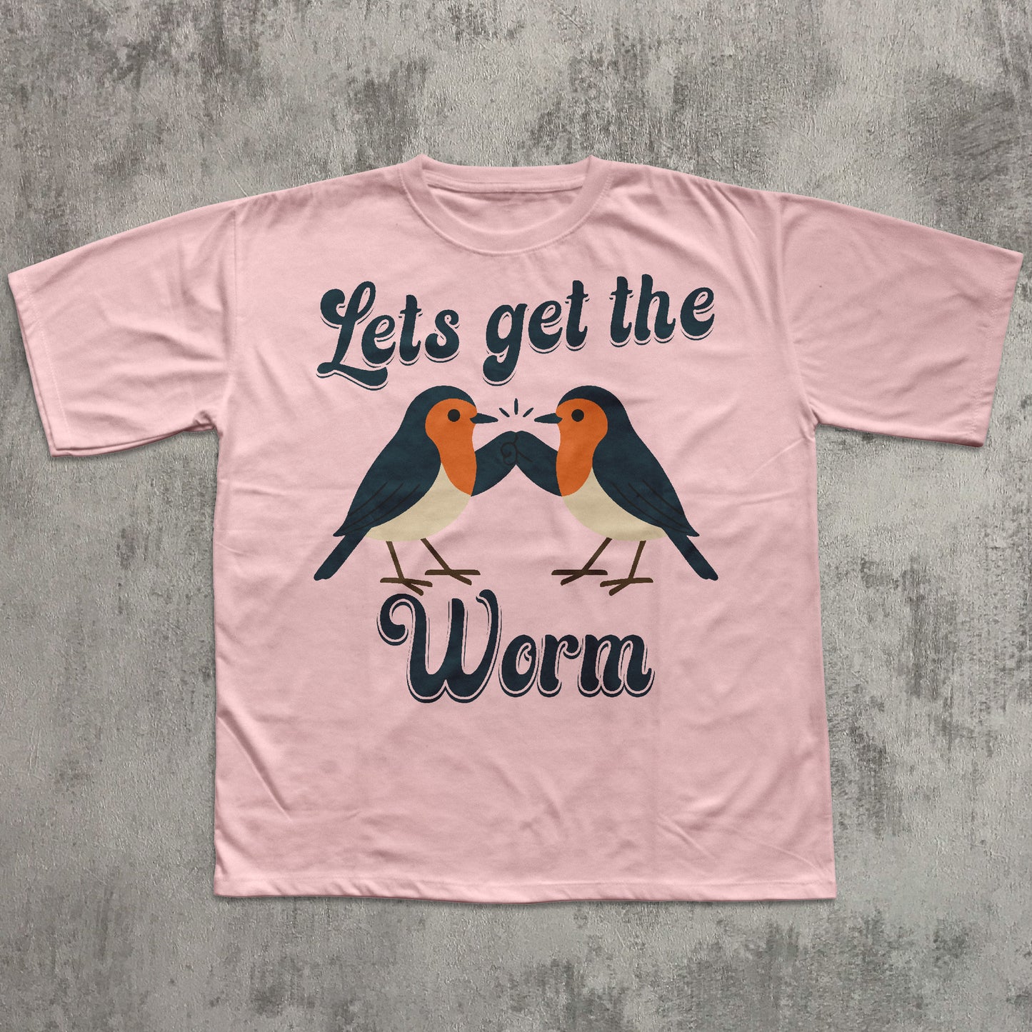 Pink t-shirt with birds and text 'Let's get the worm' on a concrete surface