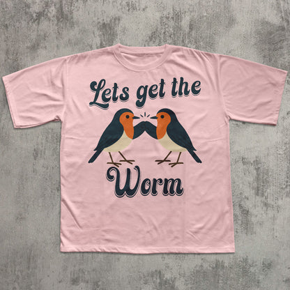 Pink t-shirt with birds and text 'Let's get the worm' on a concrete surface