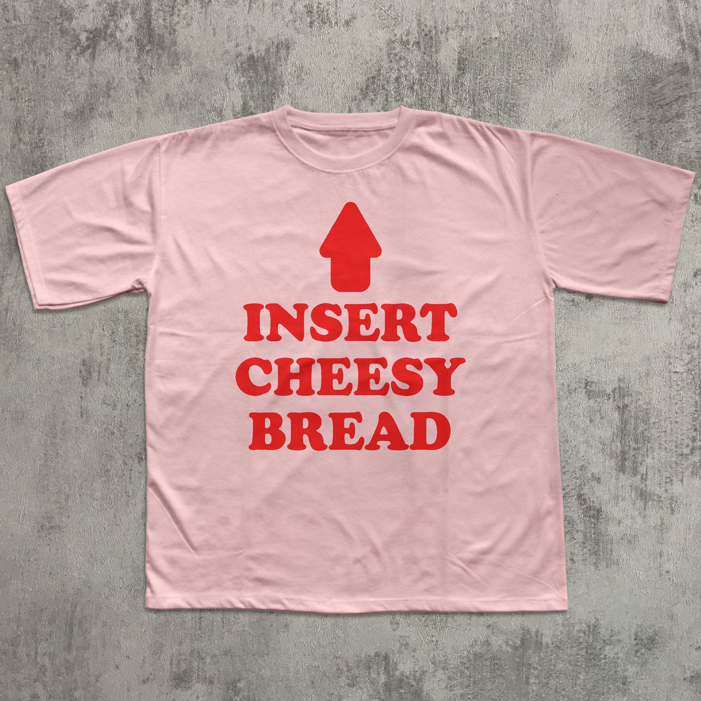 Pink t-shirt with red text 'INSERT CHEESY BREAD' on a gray textured background