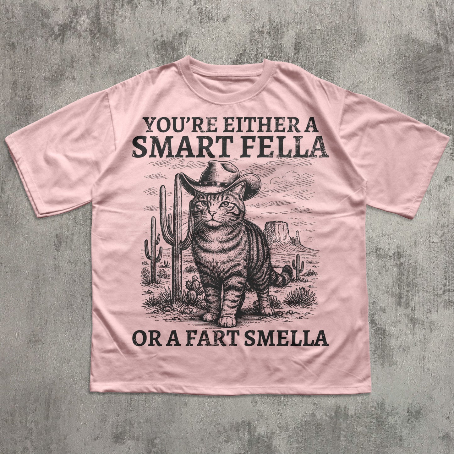 Pink t-shirt with a graphic of a cat in a cowboy hat and text on a concrete background