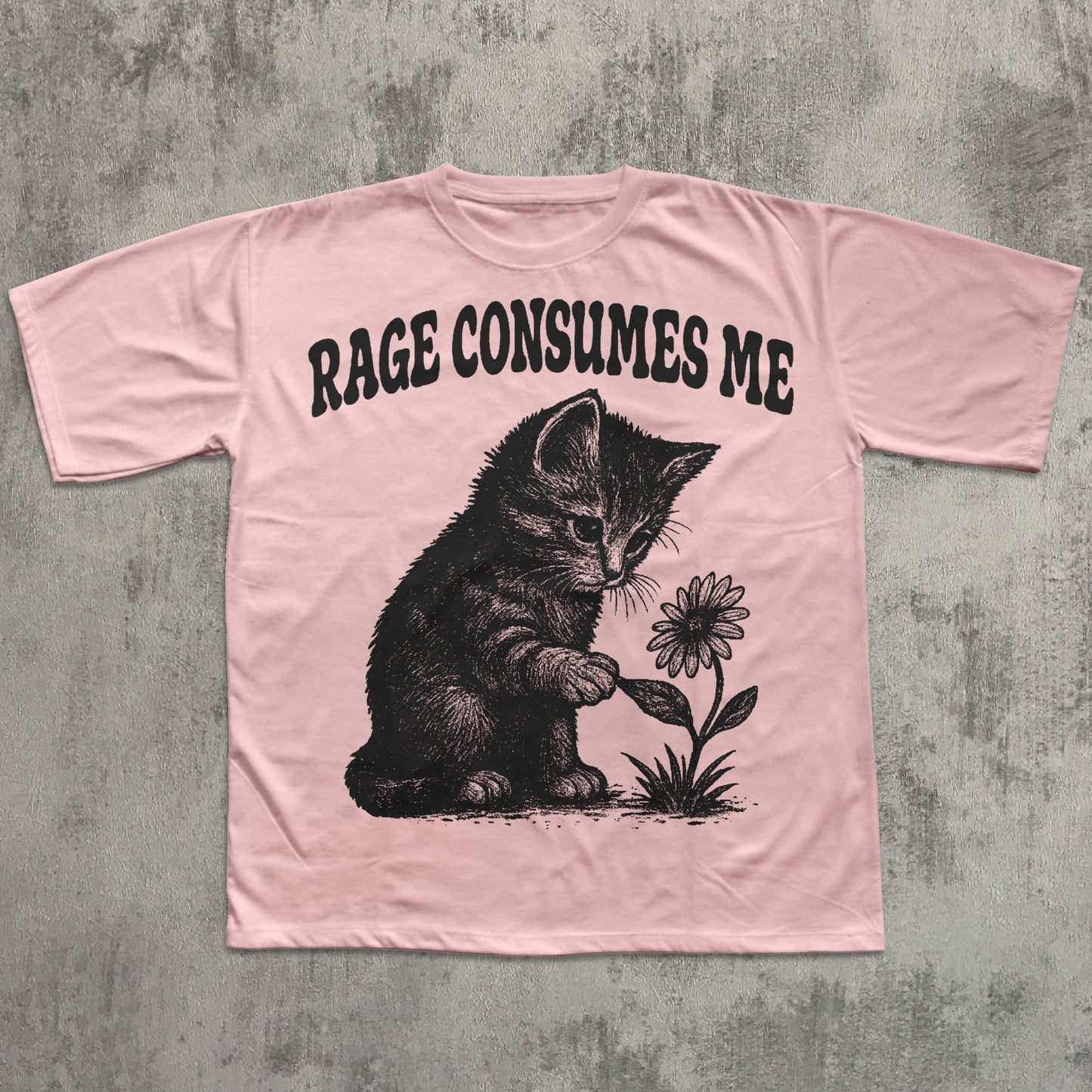 Pink t-shirt with a graphic of a cat holding a flower and text 'RAGE CONSUMES ME' on a concrete background.