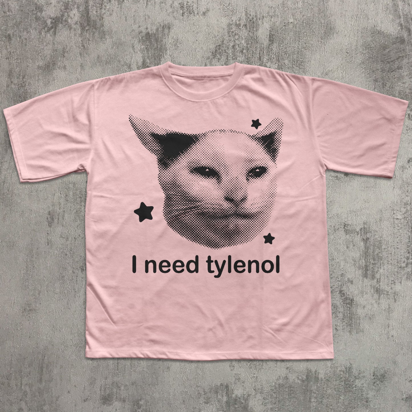 Pink t-shirt with a cat graphic and text 'I need tylenol' on a textured gray background