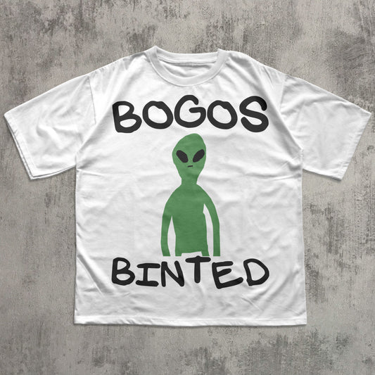 White t-shirt with green alien graphic and text 'BOGOS BINTED' on a concrete surface