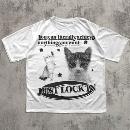 White t-shirt with a cat graphic and motivational text on a textured gray background