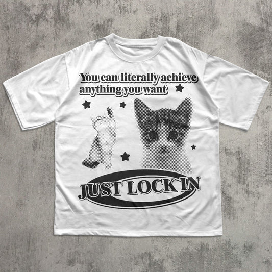 White t-shirt with a cat graphic and motivational text on a textured gray background