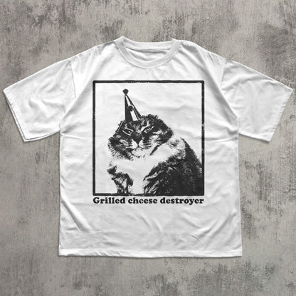 White t-shirt with a graphic of a cat wearing a cone and 'Grilled cheese destroyer' text on a concrete surface.