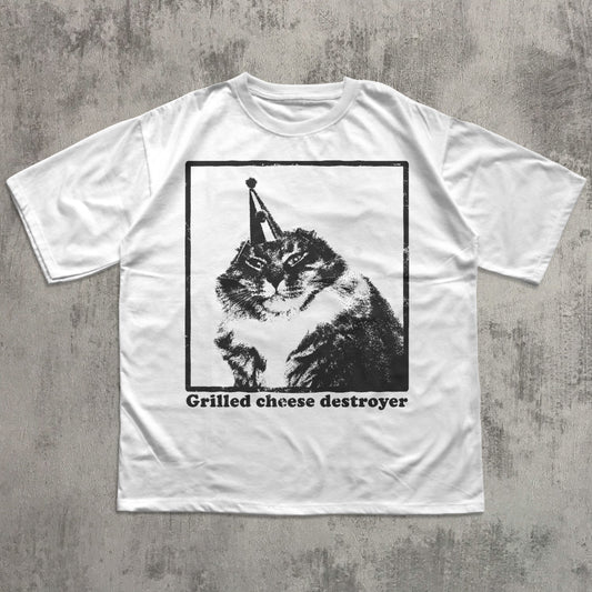 White t-shirt with a graphic of a cat wearing a cone and 'Grilled cheese destroyer' text on a concrete surface.