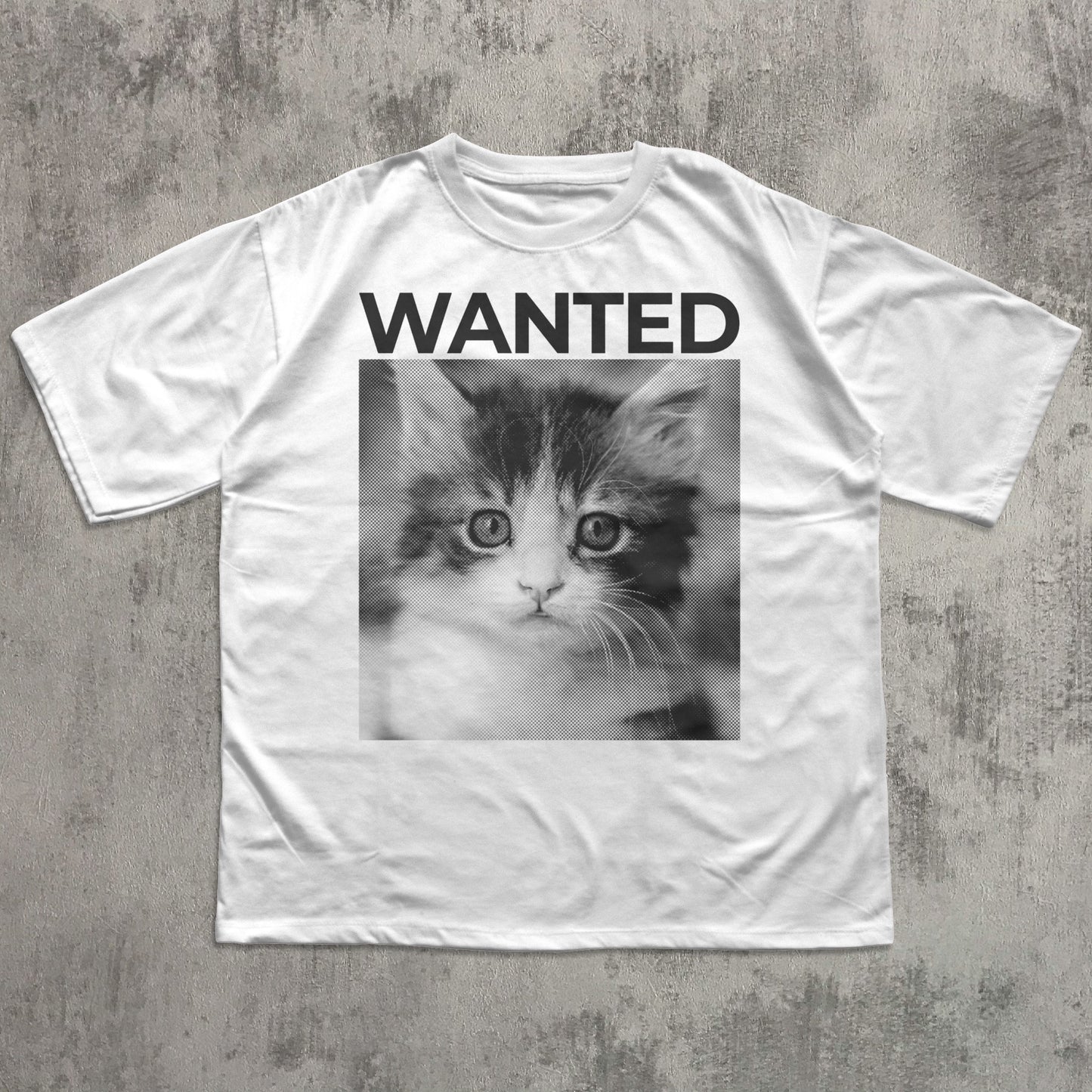 White t-shirt with a kitten graphic and 'WANTED' text on a concrete surface