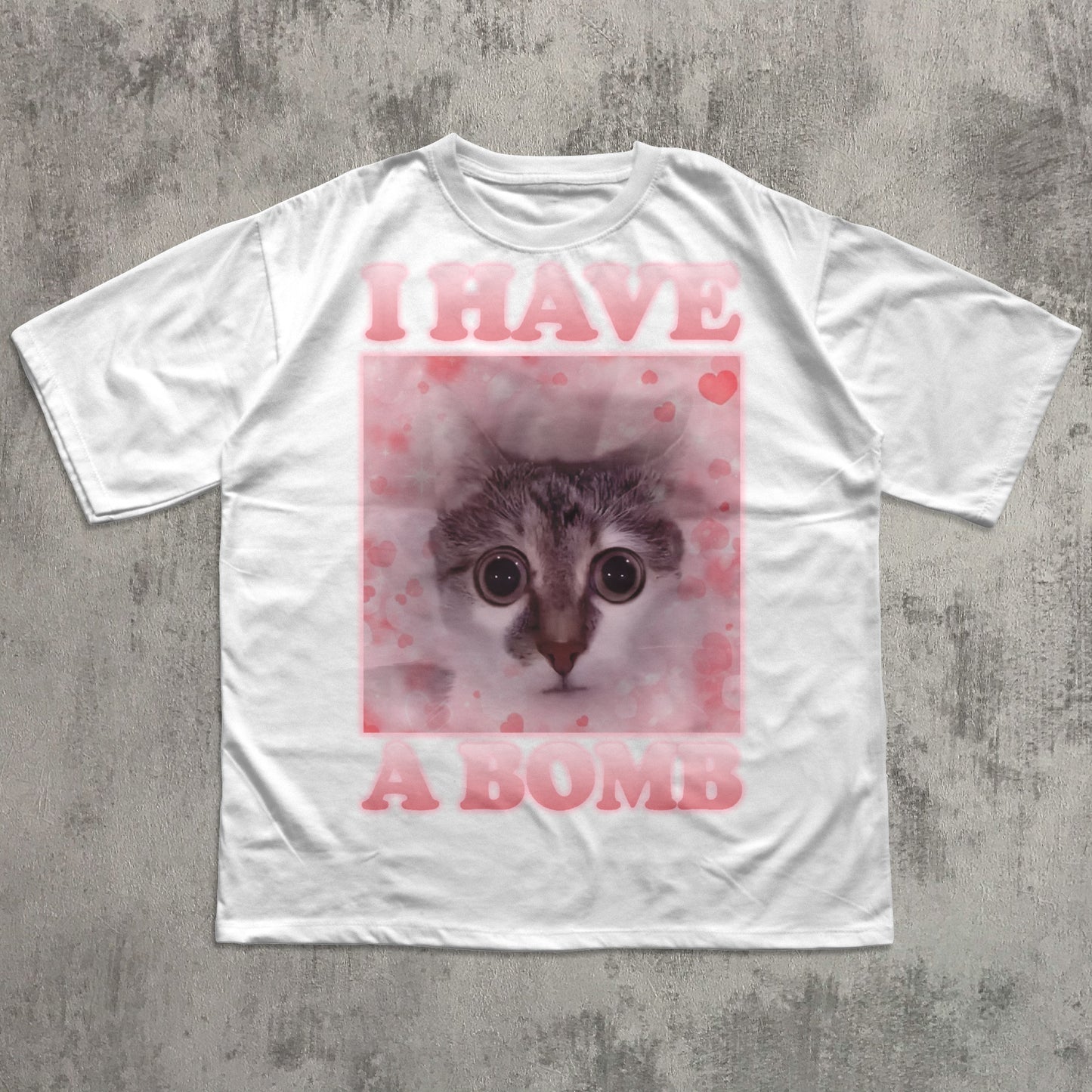 White t-shirt with a graphic of a cat and text 'I HAVE A BOMB' on a concrete surface