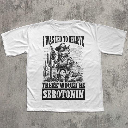 White t-shirt with a graphic design of a frog in a cowboy hat and boots, holding a rifle, with text on a concrete background.