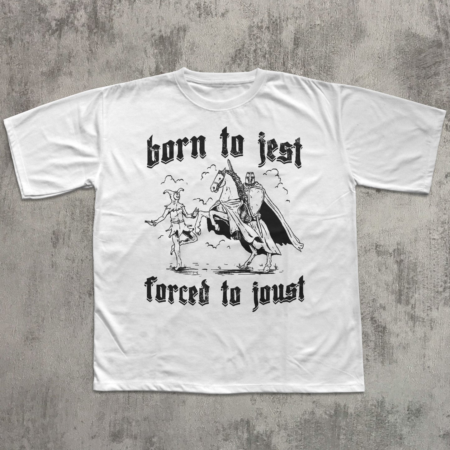 White t-shirt with black graphic and text 'born to jest, forced to joust' on a textured gray background