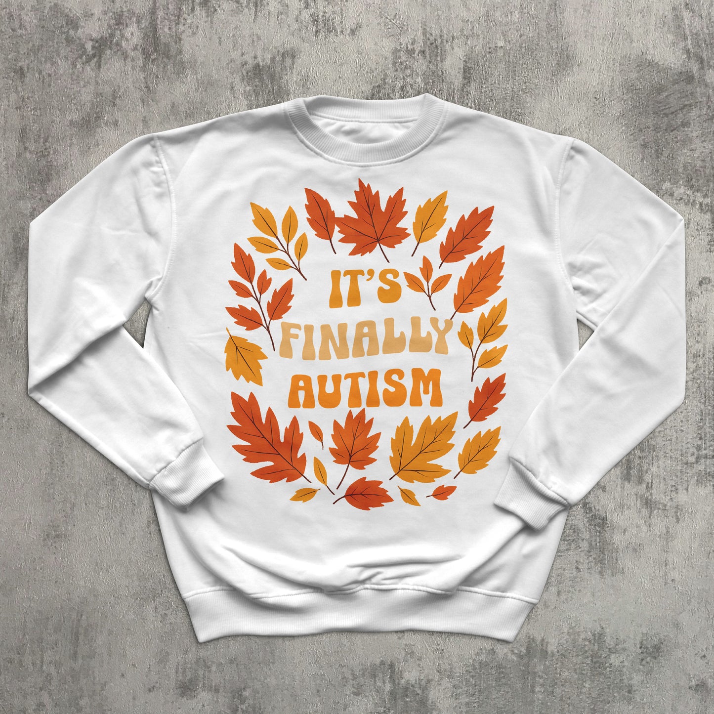 White sweatshirt with autumn leaf design and text 'It's Finally Autism' on a gray concrete background