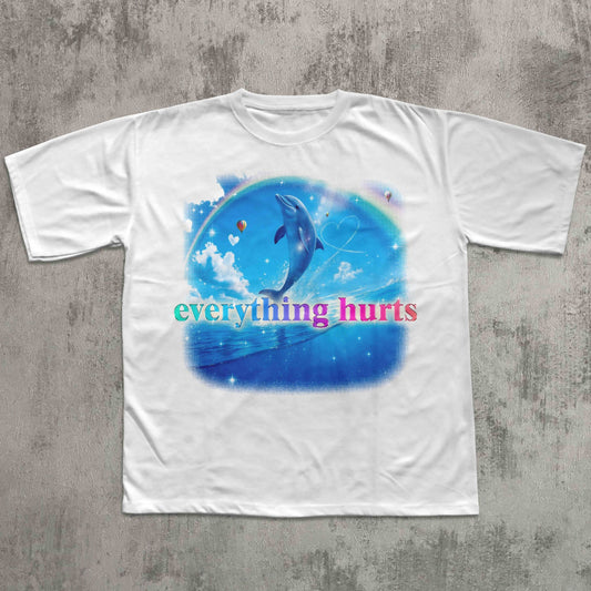 White t-shirt with a dolphin graphic and 'everything hurts' text on a textured gray background