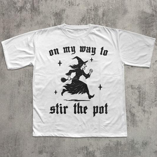 White t-shirt with black witch graphic and text on a gray concrete background