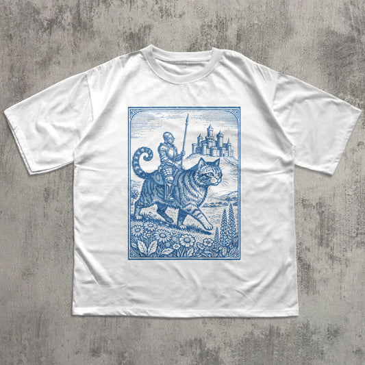 White t-shirt with blue graphic of a cat and a castle on a concrete surface
