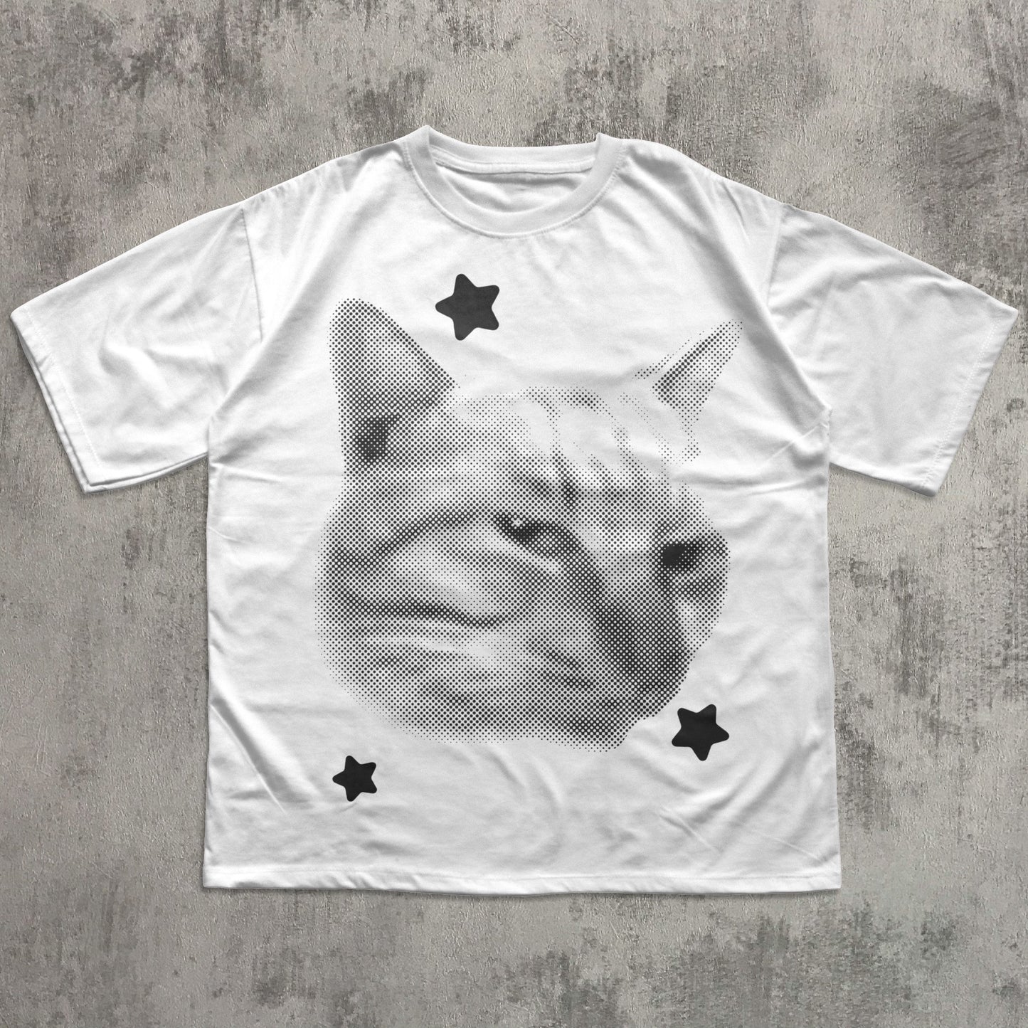 White t-shirt with a cat graphic and black stars on a gray concrete surface