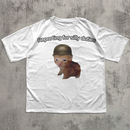 White t-shirt with a Cat wearing a helmet and text 'Reporting for silly duties' on a concrete surface.